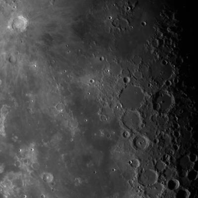 A zoomed in section of the Moon. The surface is shades of light and dark grey with many craters that range in size.