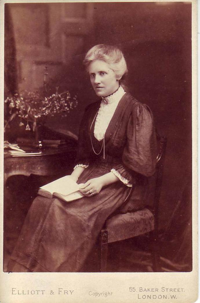 A photograph of Annie Maunder sat on a chair with a book in her hands.