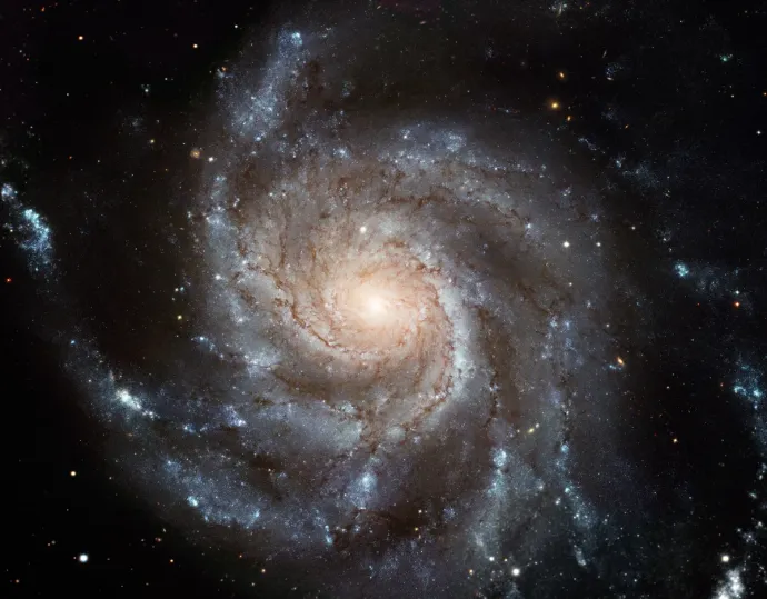 A spiral galaxy. There is a bright yellow-orange sphere in the middle with a glow around it. From this, blue-grey clouds swirl outwards, forming the spiral arms. Dots of stars are visible in the arms, mostly bright white and blue in colour, but some further out from the centre are more reddish in colour. There are also stars against the black background.